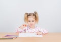 Little girl draws at table pencils.