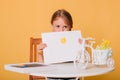 Little girl draws on a white sheet of paper. A creative child shows the sun hatch. Studio photo on a yellow background. art Royalty Free Stock Photo