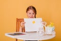 Little girl draws on a white sheet of paper. A creative child shows the sun hatch. Studio photo on a yellow background. art Royalty Free Stock Photo