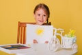 Little girl draws on a white sheet of paper. A creative child shows the sun hatch. Studio photo on a yellow background. art Royalty Free Stock Photo