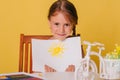 Little girl draws on a white sheet of paper. A creative child shows the sun hatch. Studio photo on a yellow background. art Royalty Free Stock Photo