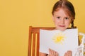 Little girl draws on a white sheet of paper. A creative child shows the sun hatch. Studio photo on a yellow background. art Royalty Free Stock Photo