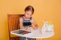 Little girl draws on a white table with crayons. Creative child. Studio photo on a yellow background. Art Royalty Free Stock Photo