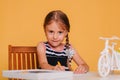 Little girl draws on a white table with crayons. Creative child. Studio photo on a yellow background. Art Royalty Free Stock Photo