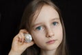 Little girl is dreaming about the summer trip to the ocean and listening to a white shell to hear a sea sound on black Royalty Free Stock Photo