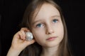 Little girl is dreaming about the summer trip to the ocean and listening to a white shell to hear a sea sound on black Royalty Free Stock Photo