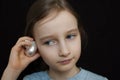 Little girl is dreaming about the summer trip to the ocean and listening to a white shell to hear a sea sound on black Royalty Free Stock Photo