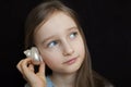 Little girl is dreaming about the summer trip to the ocean and listening to a white shell to hear a sea sound on black Royalty Free Stock Photo