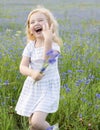 A little girl in a dress and with a bouquet of flowers laughs and plays in a field with cornflowers on a summer day