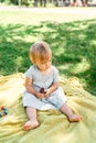 Little girl in a dress with ice cream in her hand sits on a bedspread on a green lawn Royalty Free Stock Photo