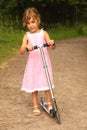 Little girl in dress rides scooter on nature Royalty Free Stock Photo