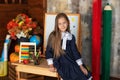 A little girl in dress sit on table in classroom. School child sitting at wooden desk in front of chalkboard. Royalty Free Stock Photo