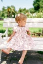 Little girl in a dress sits on a bench and holds a leaf in her hand