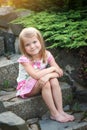 A little girl in a dress sits on the stone steps in the garden. Bare feet, smile Royalty Free Stock Photo