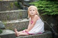 A little girl in a dress sits on the stone steps in the garden. Bare feet, smile Royalty Free Stock Photo