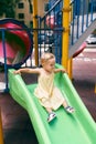 Little girl in a dress slides down a slide on the playground Royalty Free Stock Photo