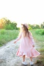 Little girl in dress and straw hat is walking along country road. Happy childhood. Summer vacation. Kid walks along rural road on Royalty Free Stock Photo