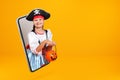 A little girl dressed as a pirate for Halloween holds a bucket with a pumpkin lantern and looks from a smartphone. Royalty Free Stock Photo