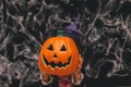Little girl dressed as a witch holding a pumpkin against a dark background with spiderwebs