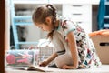 Little girl dressed in the dress and tights draws in the album sitting on the floor in the room