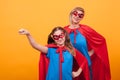 Little girl dressed like superheros holding her fist up in the air with her mother over eyellow background.