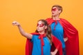 Little girl dressed like superheros holding her fist up in the air with her mother over eyellow background.