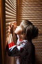 Little girl dressed in the pajama is hiding in the closet with wooden doors Royalty Free Stock Photo