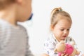 Little girl dressed in white clothes playing with toys sitting on the bed indoors. Beautiful little girl of Slavic Royalty Free Stock Photo