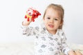 Little girl dressed in white clothes playing with toys sitting on the bed indoors. Beautiful little girl of Slavic Royalty Free Stock Photo