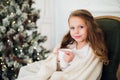 Little girl drinking milk near Christmas tree in morning at home Royalty Free Stock Photo