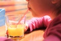 Little girl drinking orange juice using straw in cafe and looks thoughtfully out the window Royalty Free Stock Photo