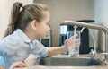 Little girl drinking from water tap or faucet in kitchen. Pouring fresh drink. Healthy lifestyle. Water quality check concept. Royalty Free Stock Photo