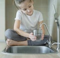 Little girl drinking from water tap or faucet in kitchen. Pouring fresh drink. Healthy lifestyle. Water quality check concept. Royalty Free Stock Photo