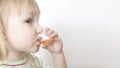 Little girl drinks cough syrup in a measuring cup for children. The concept of treating bronchitis and pneumonia with drug syrup