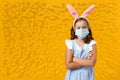 Little girl in the ears of an Easter bunny in a protective medical mask on a yellow background. Royalty Free Stock Photo