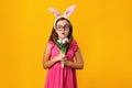 Little girl in ears and glasses of Easter bunny on a yellow background. The child is holding a bouquet of tulips Royalty Free Stock Photo