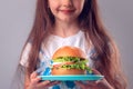 Little girl eating big burger. Kid looking at healthy big sandwich, studio isolated on white background Royalty Free Stock Photo