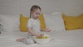 little girl eating golden potato chips sitting on the bed in the bedroom, fast food for kid, unhealthy baby food Royalty Free Stock Photo