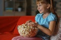 Little girl eating popcorn while watching TV on sofa in evening Royalty Free Stock Photo