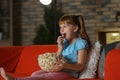 Little girl eating popcorn while watching TV on sofa in evening Royalty Free Stock Photo