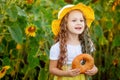 A little girl eats a bagel in a field with sunflowers in summer Royalty Free Stock Photo