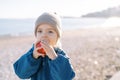 Little girl eats a big red apple holding it in her hands while standing on a sandy beach Royalty Free Stock Photo