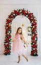 A little girl in a elegant pink dress is dancing in a room against the background of a Christmas arch