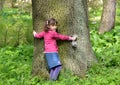 The little girl embraces a trunk of a big tree