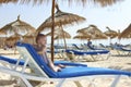 A little girl of European appearance in a striped pink swimsuit is lying on a deck chair under an umbrella on the beach Royalty Free Stock Photo