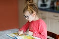 Little girl with eyeglasses learning reading. Child of elementary school reads a book at home, making school homework. Royalty Free Stock Photo