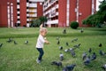 Little girl feeds bread to pigeons on a green lawn in front of an apartment building Royalty Free Stock Photo