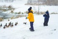 Little girl feeds the hungry ducks on a frozen lake