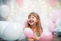 Little girl, in festive clothes and tiara, sits against background balloons