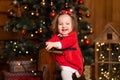 Little girl in a festive red dress on a wooden swing rocking horse. Christmas parties are a fabulous time for children